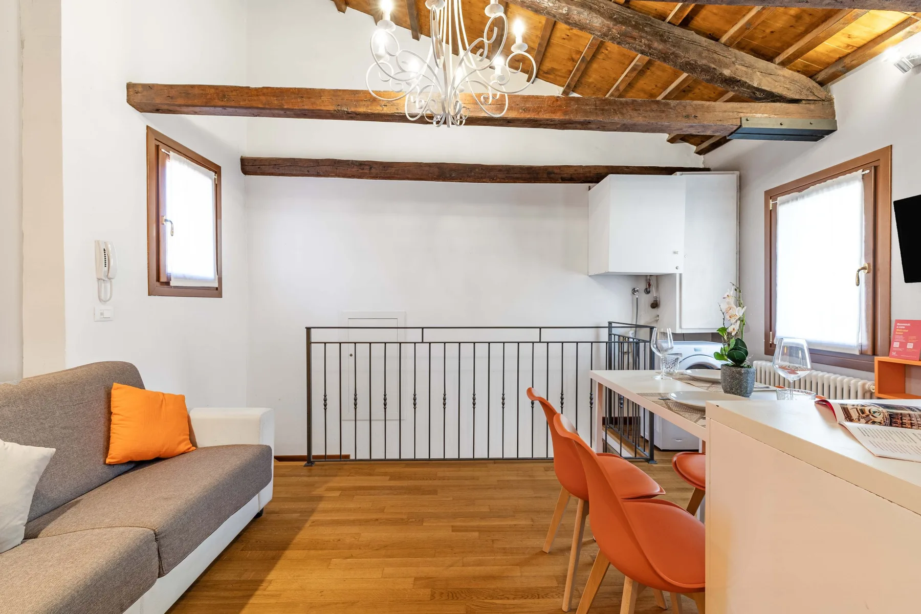Una sala luminosa con un sofá gris, asientos naranjas y techo de madera.