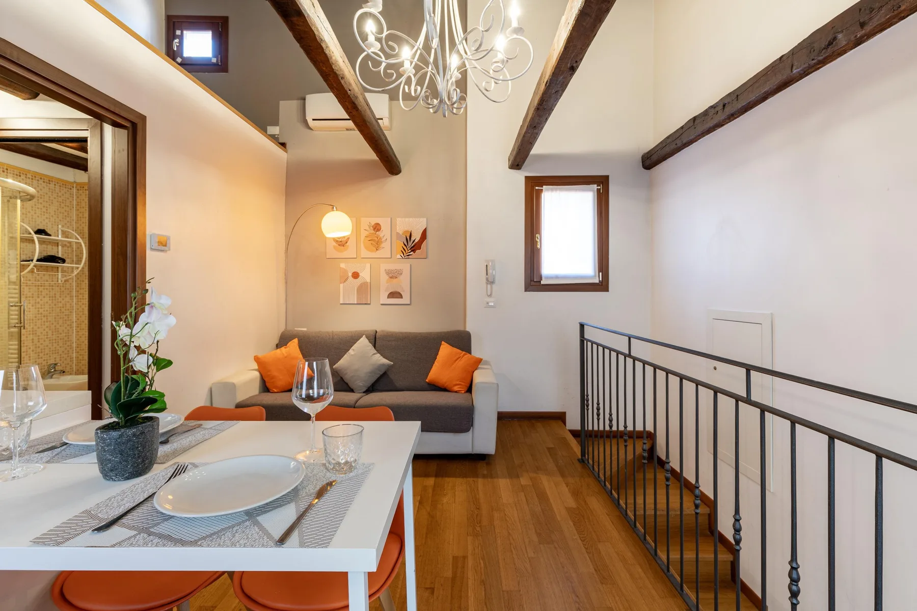 Zona de estar y comedor tipo loft, con sofá gris, mesa y vigas expuestas.