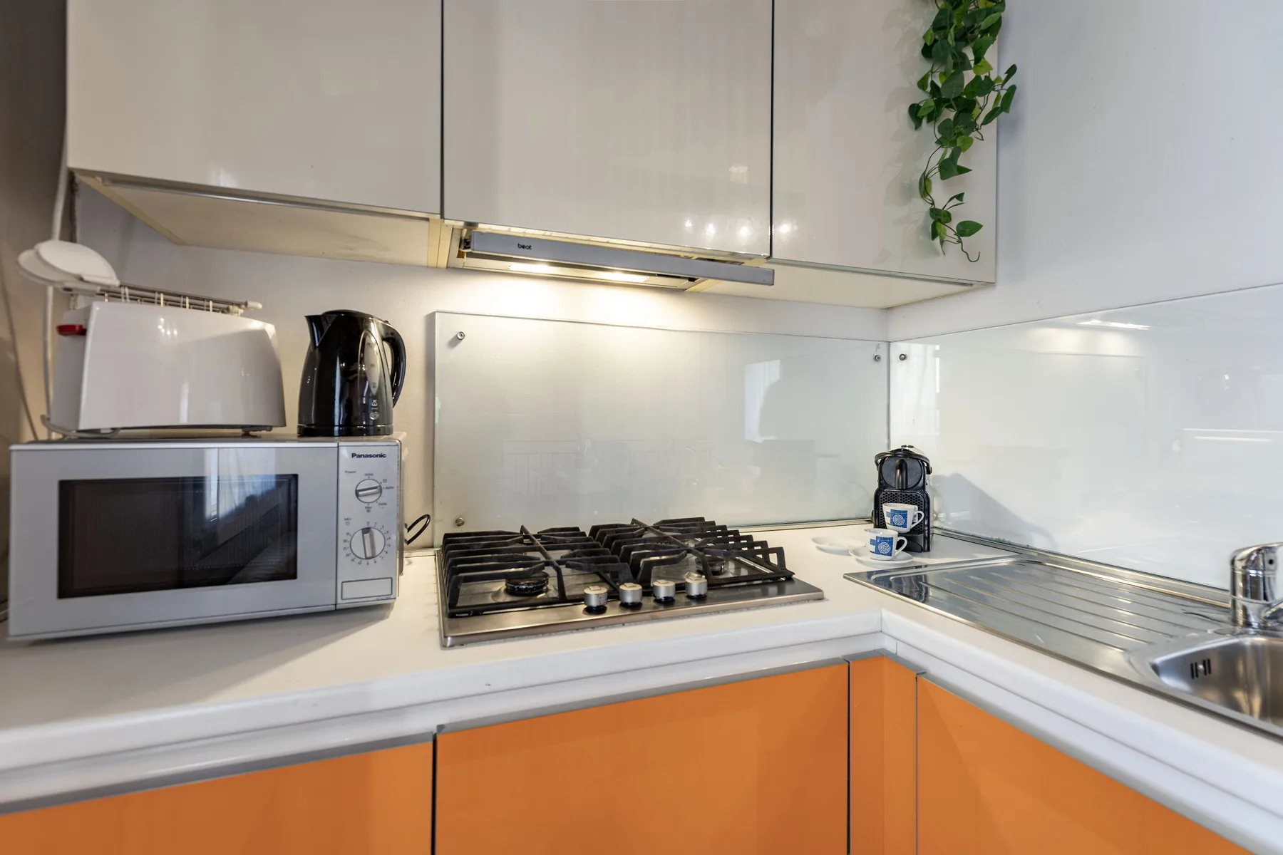 Una cocina compacta tiene una placa de gas, un microondas y un fregadero de acero inoxidable.