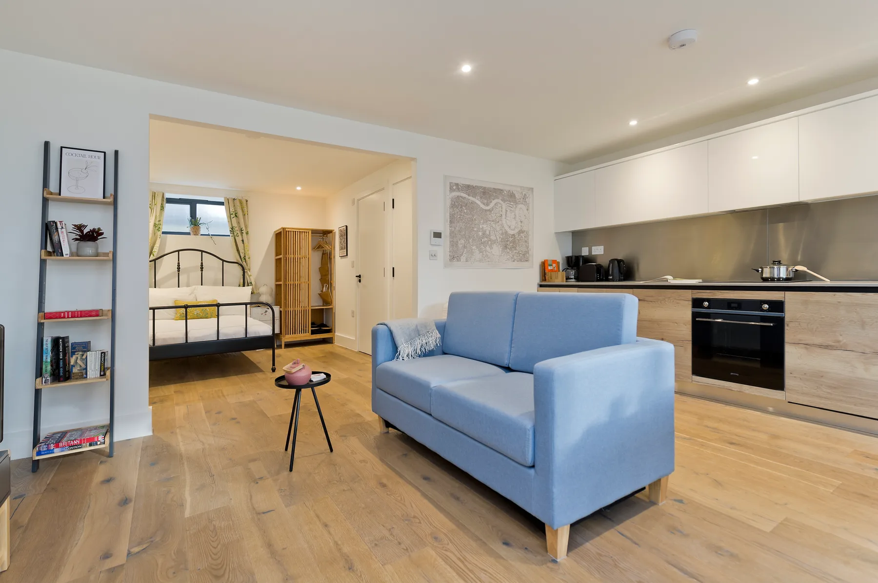 A bright open-plan room with a blue sofa, kitchen, and sleeping area.