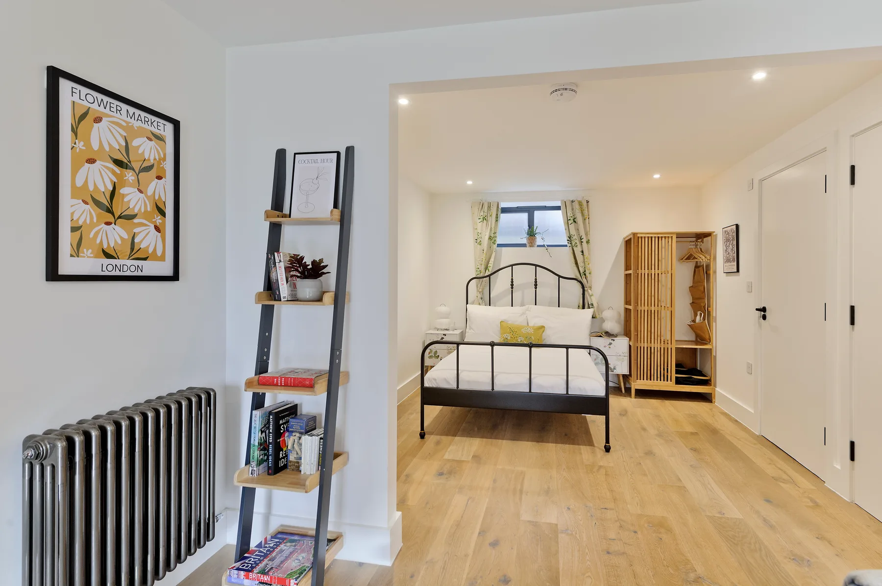A bright bedroom with a metal bed, window, and light wood flooring.