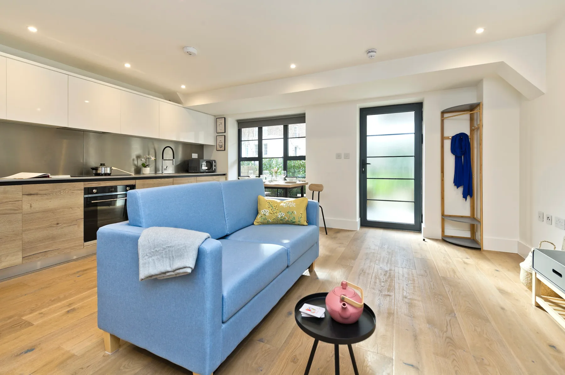 A bright open-plan living room with a blue sofa and kitchen.