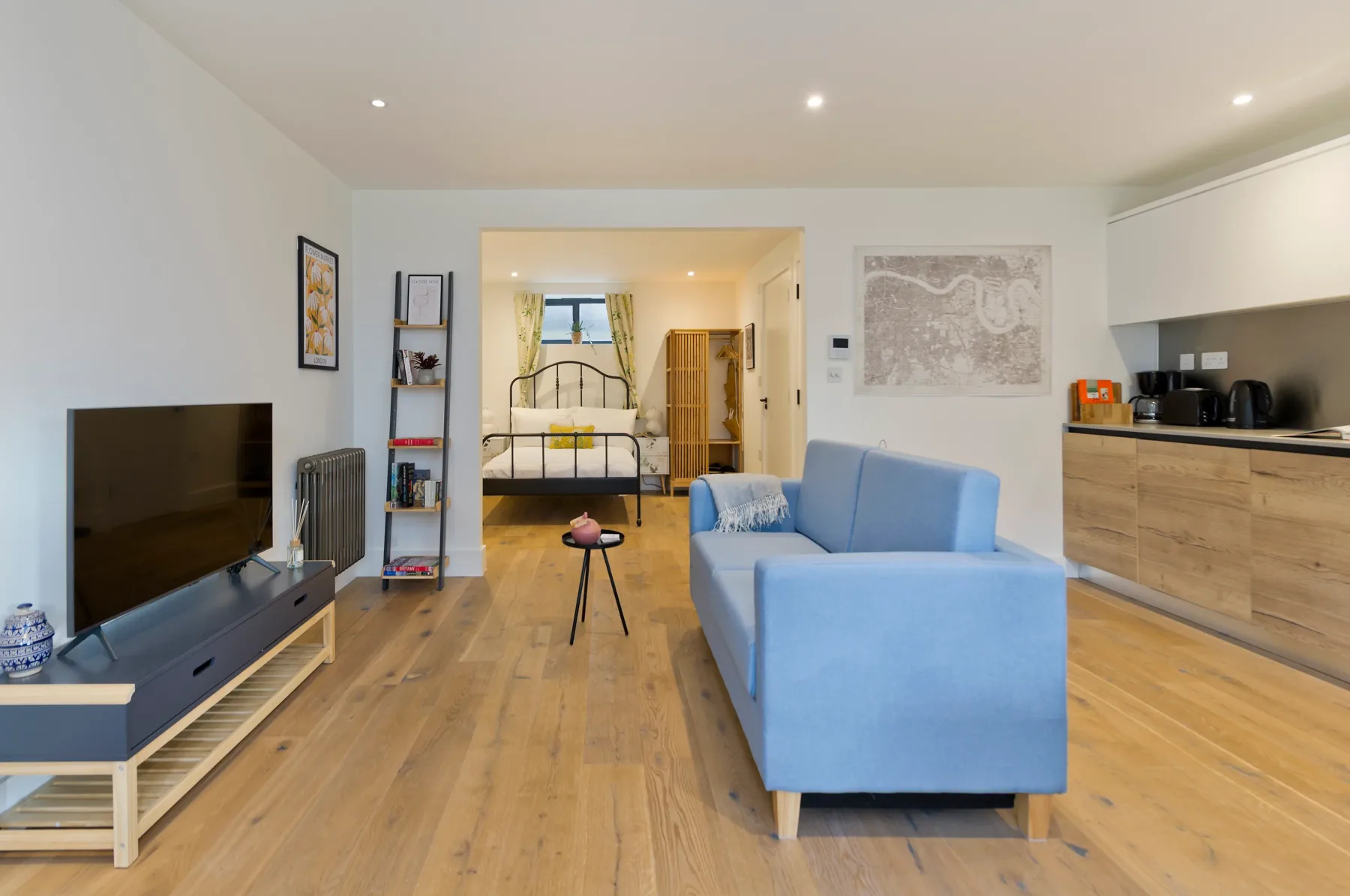A bright living area with blue seating, a television, and a kitchen along the wall.