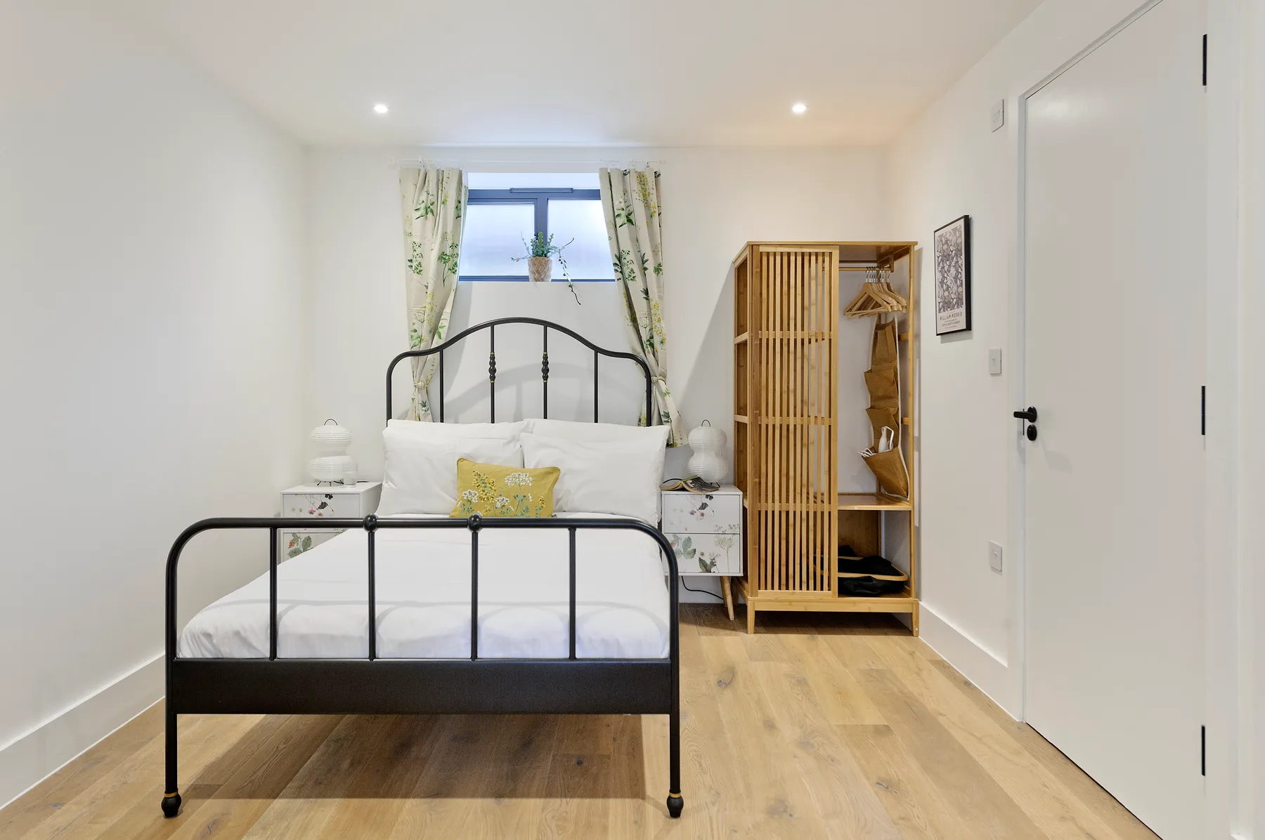 A bedroom with a metal bed, a small window, and a wooden wardrobe.