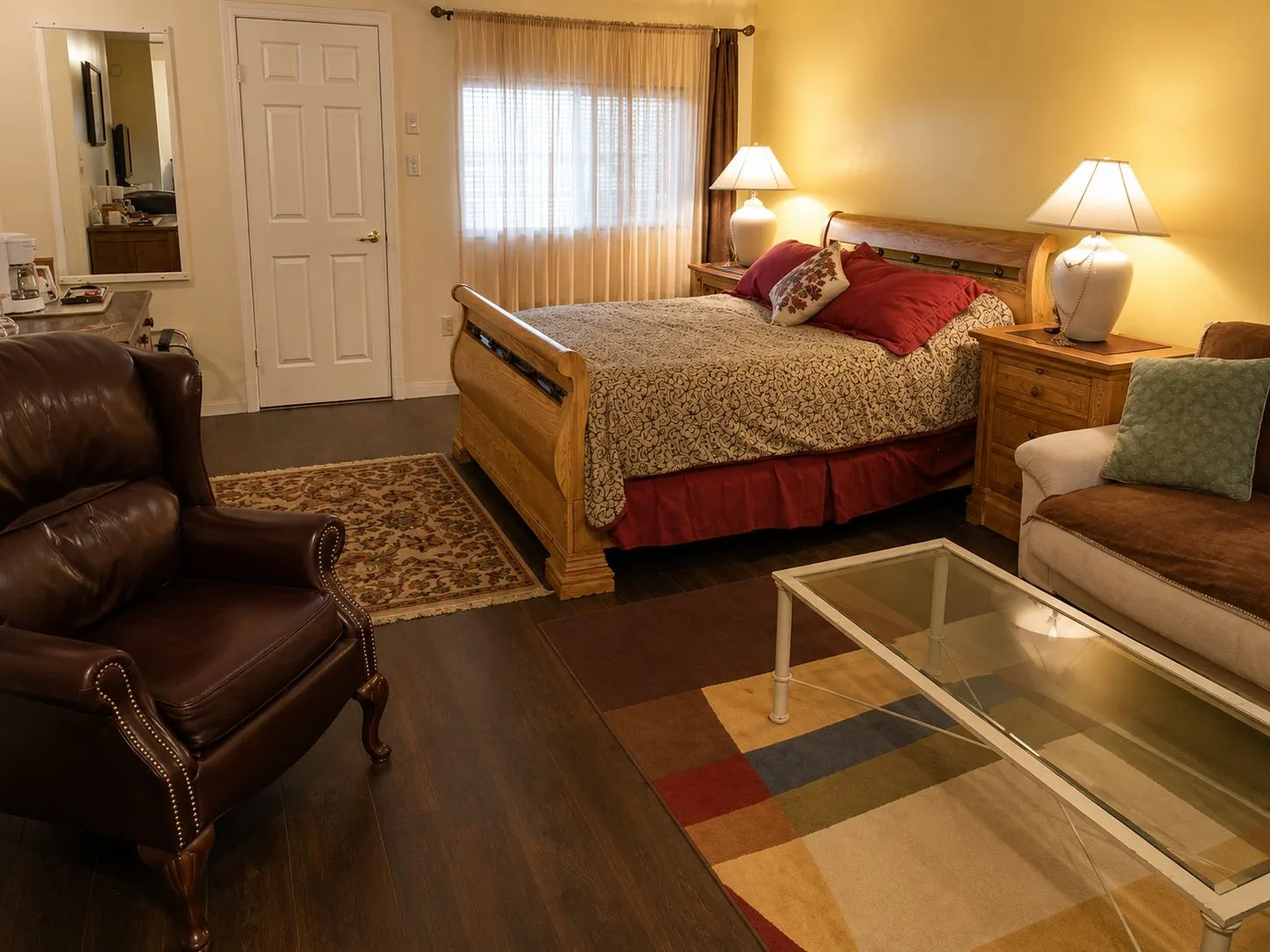 La suite Tucson: una cama queen con estructura de madera tipo trineo y lámparas a ambos lados, un sillón de cuero y un sofá en primer plano.