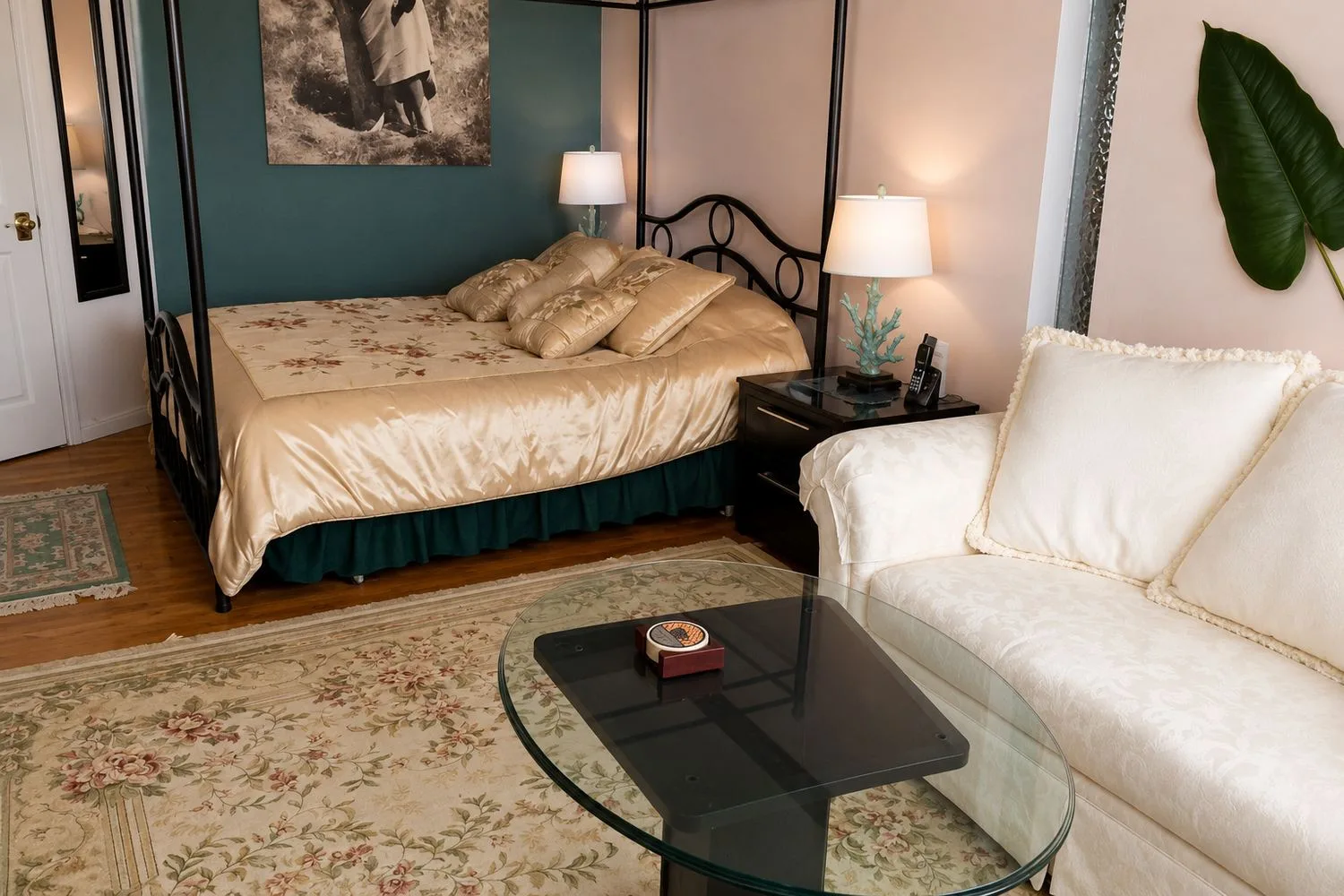 La suite Den: una cama queen en una estructura negra de cuatro postes con una colcha dorada, lámparas a ambos lados y un sofá color crema al lado.