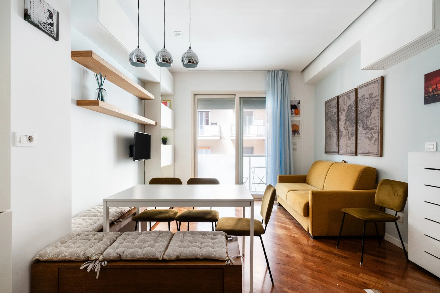 A bright living room with seating, a table, and a glass door opening to a balcony.