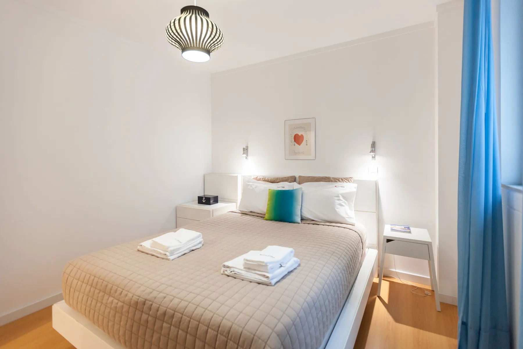 Un dormitorio luminoso con una cama bien hecha y cortinas azules.