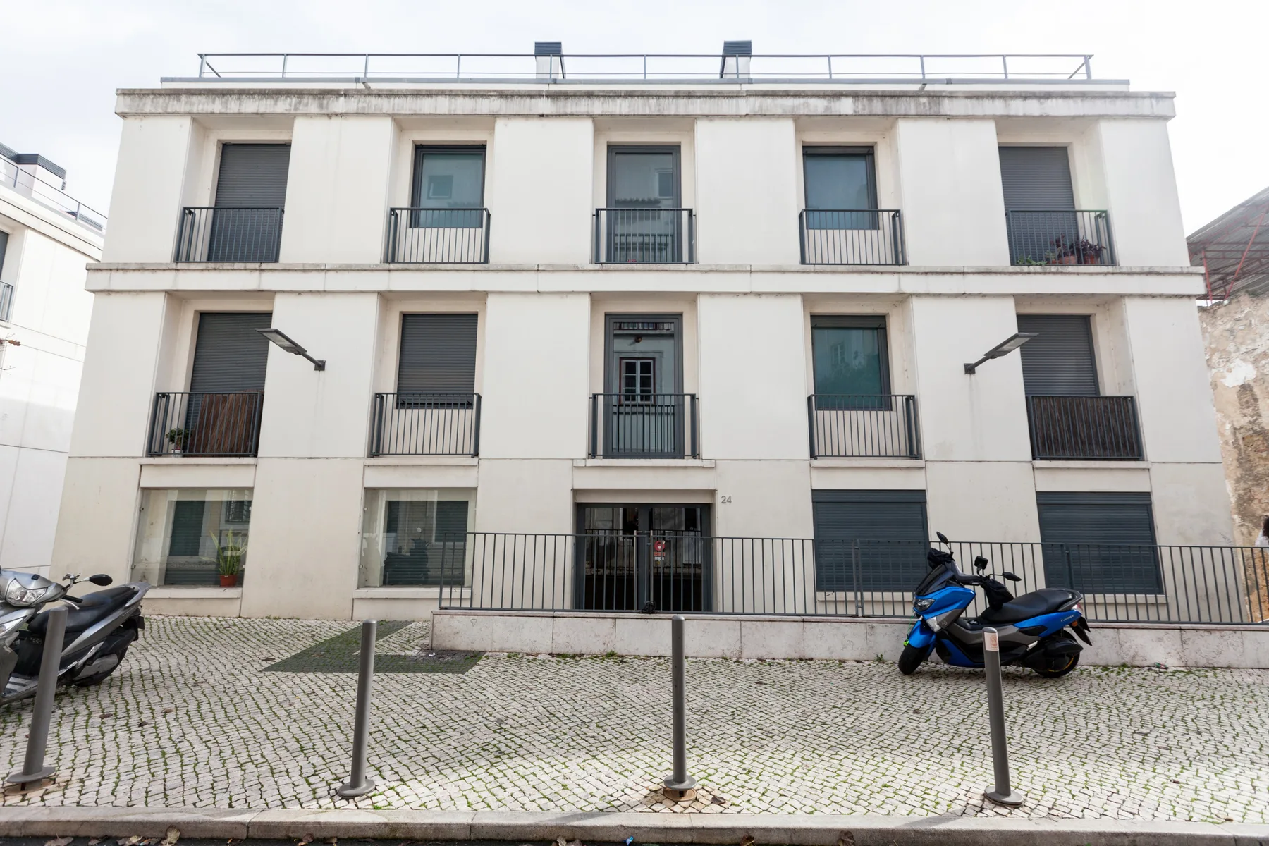 Un edificio de apartamentos blanco con balcones da a una calle empedrada.