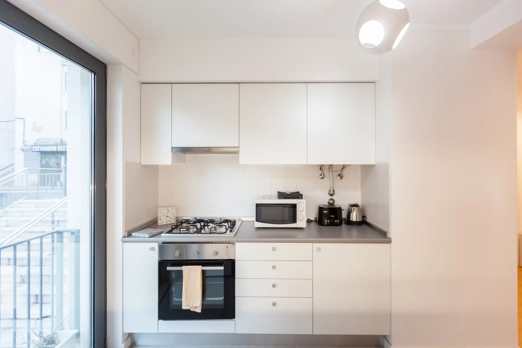 Una cocina luminosa con gabinetes blancos, una placa de cocina y electrodomésticos sobre la encimera.