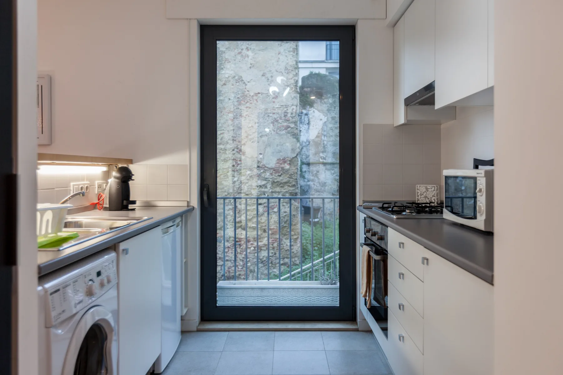 Una cocina compacta con encimeras, electrodomésticos y una puerta de vidrio que da a un pequeño balcón.
