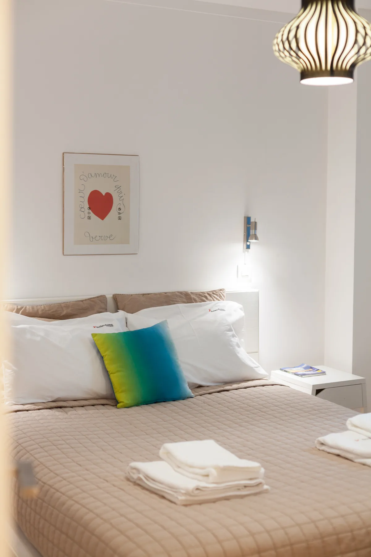 Un dormitorio con una cama bien tendida y un cojín de colores.