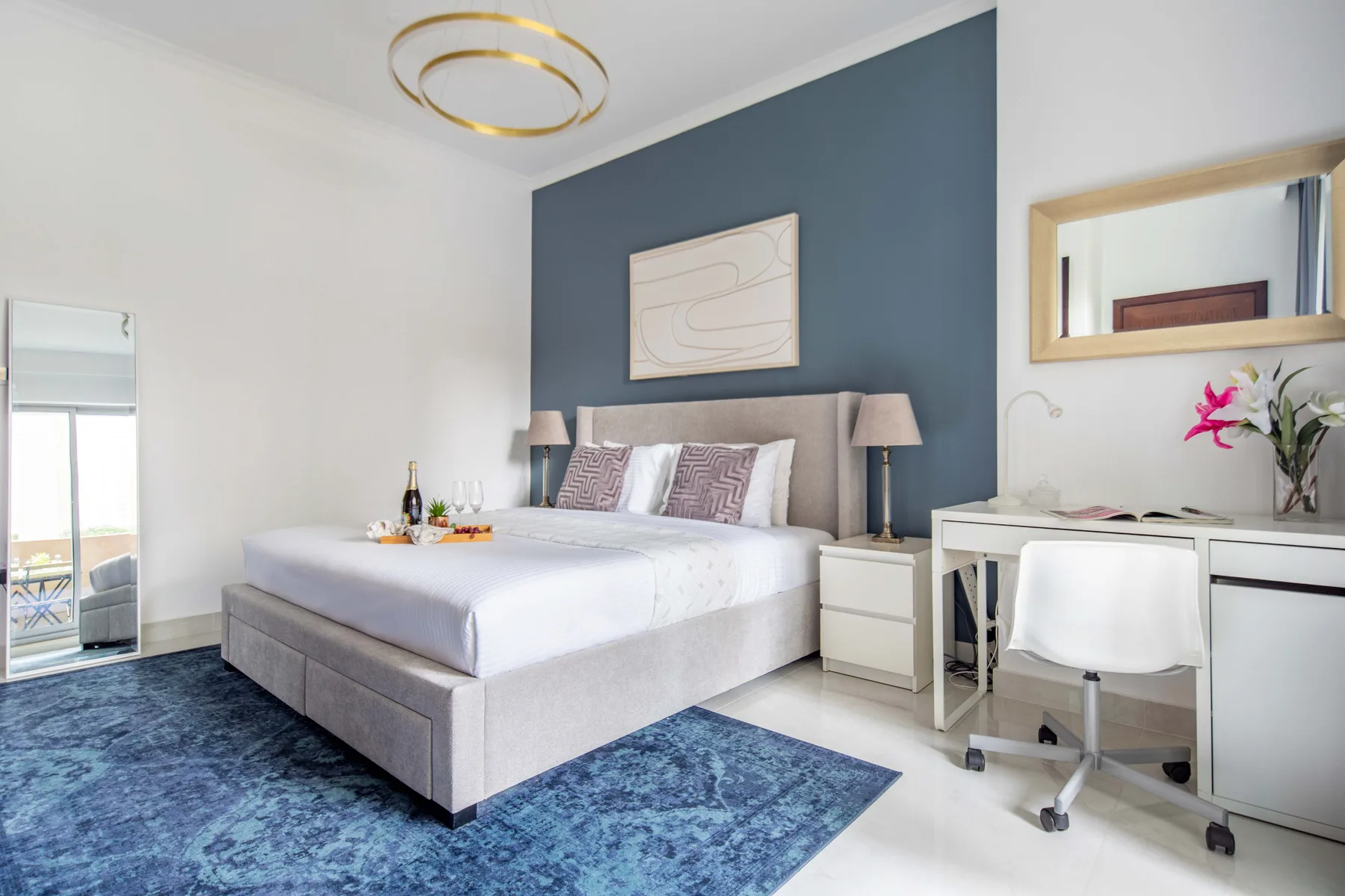 Un dormitorio con una cama grande, una pared azul y un escritorio junto a la ventana.