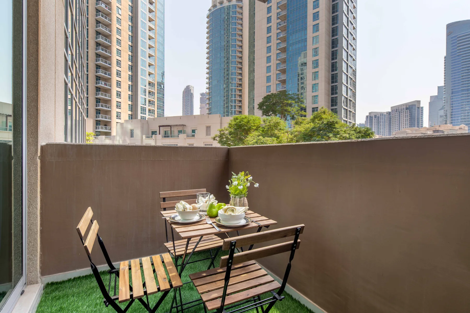 Una pequeña zona de comedor al aire libre con mesa y sillas está junto a un muro alto.