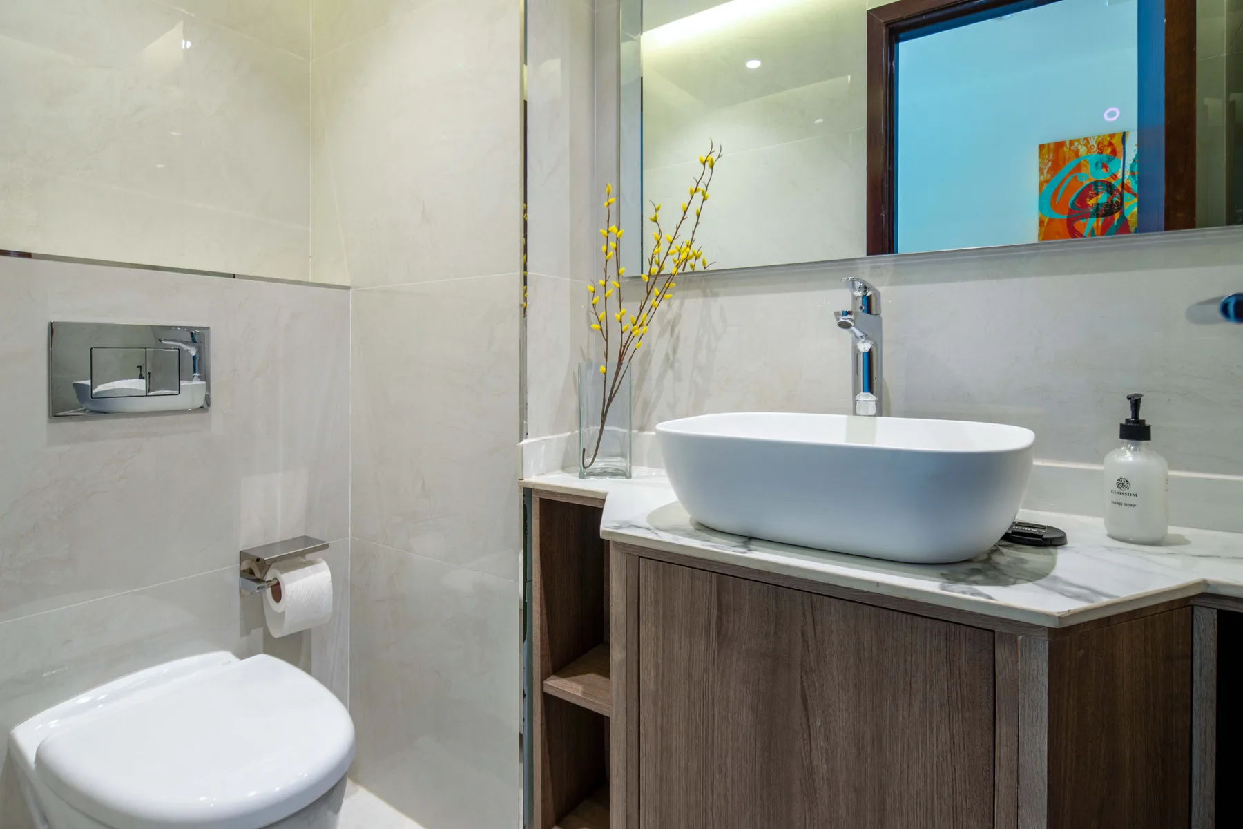 Un lavabo de baño con un lavamanos sobrepuesto y un inodoro junto a una zona de ducha revestida.