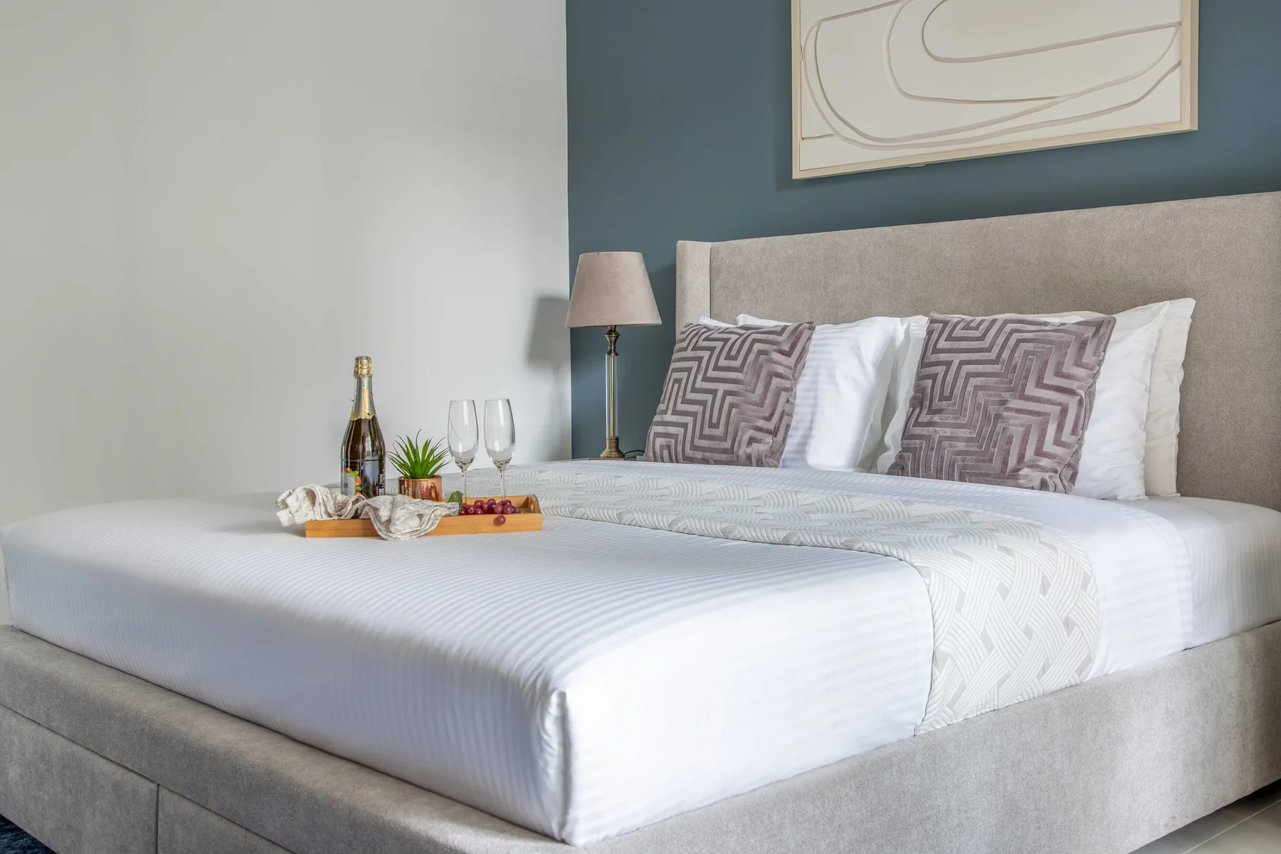 Un dormitorio con una cama bien tendida, cojines estampados y una bandeja sobre la cama.