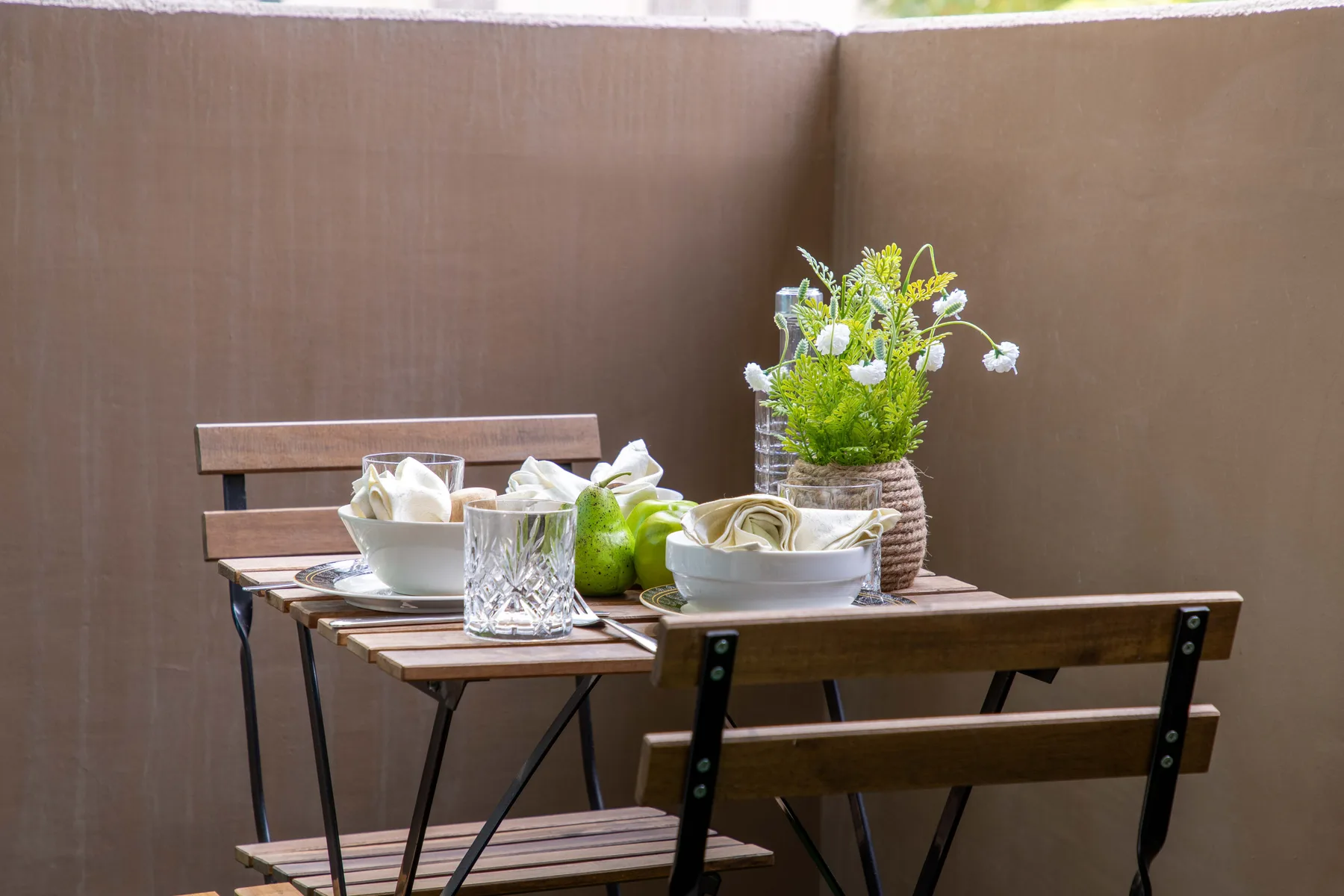 Una pequeña zona de comedor al aire libre con una mesa de madera, platos y flores.