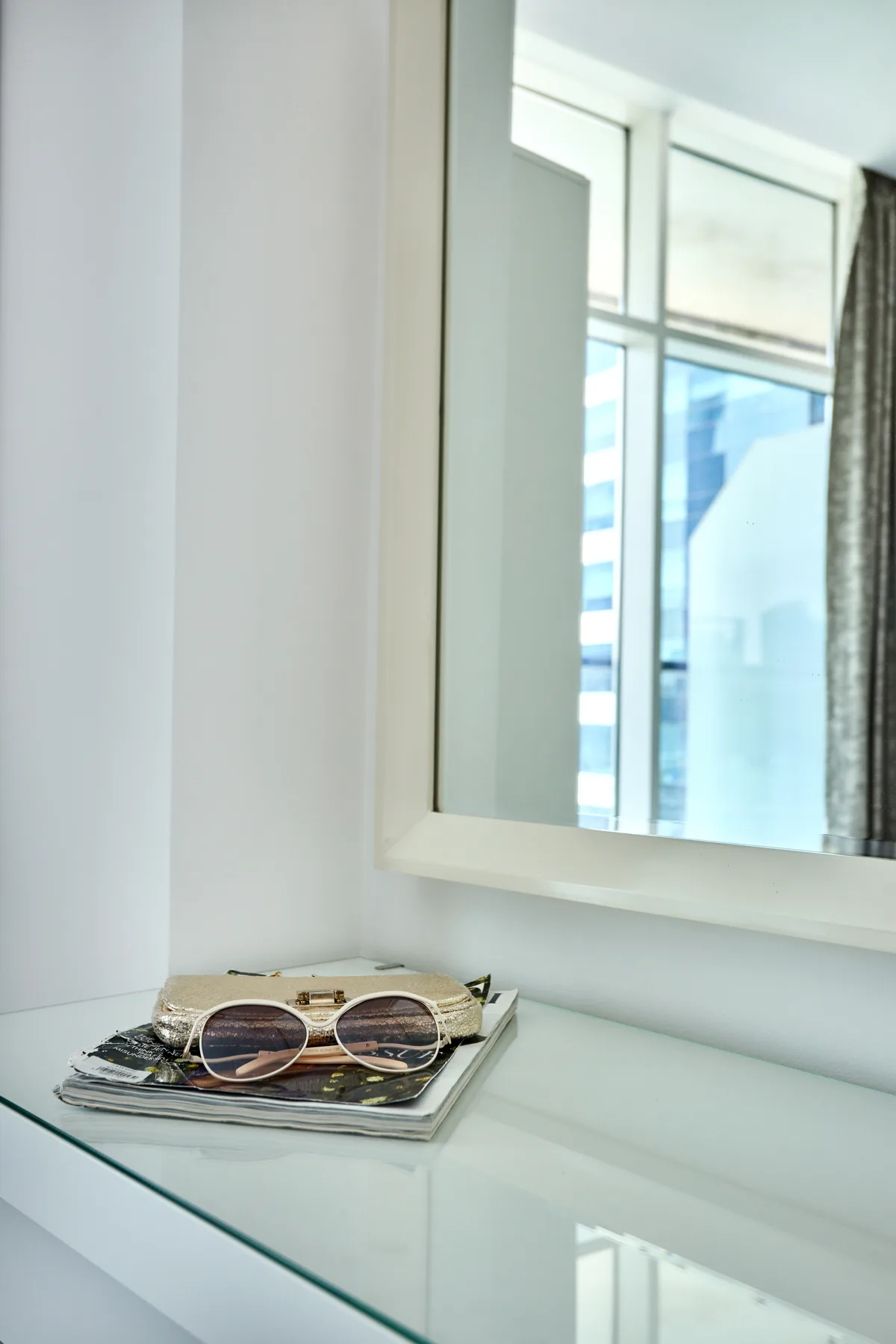 Un rincón luminoso con gafas de sol sobre una mesa de vidrio debajo de un espejo.