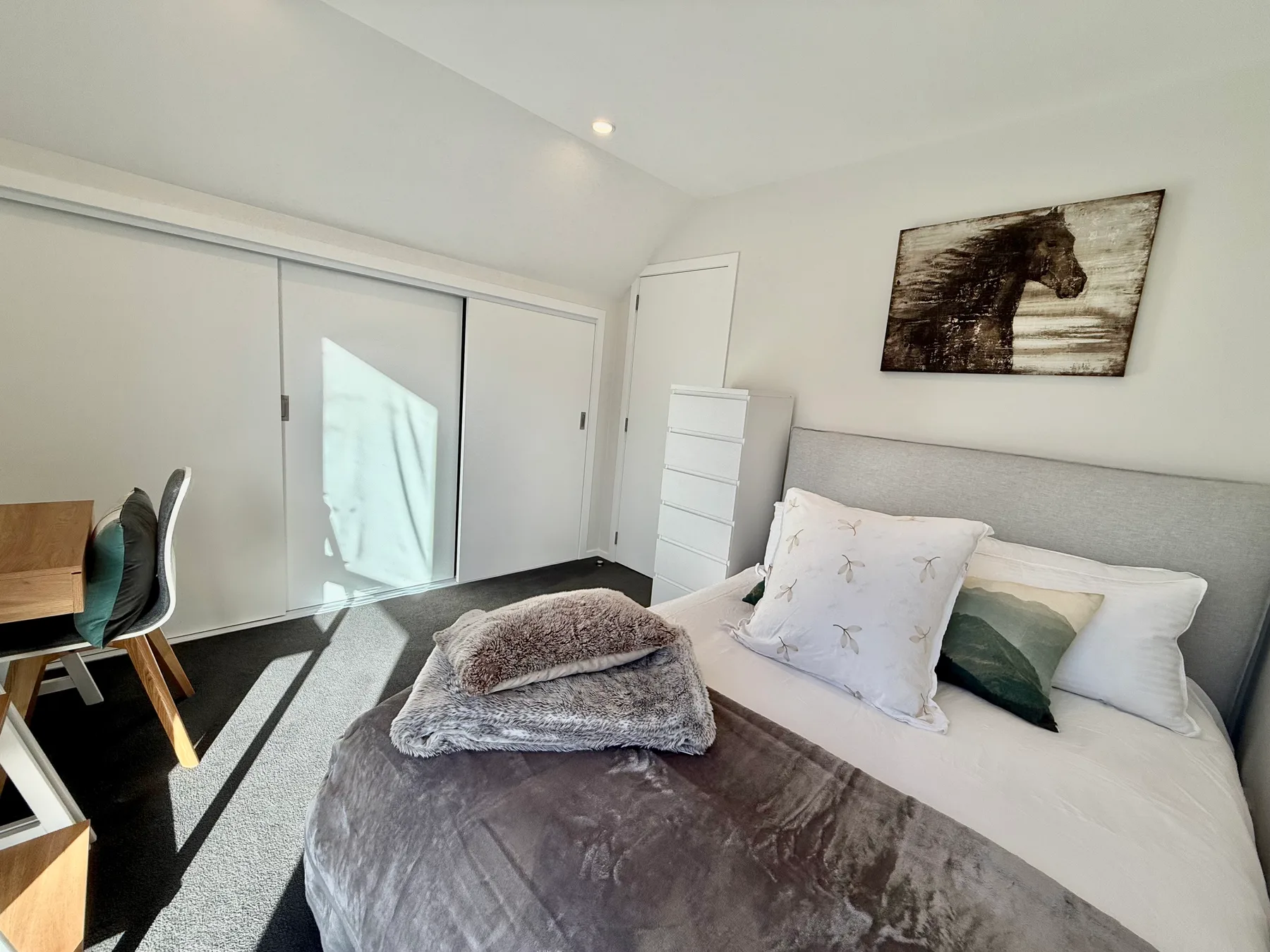 A bedroom with a bed, desk, and sliding wardrobe doors.