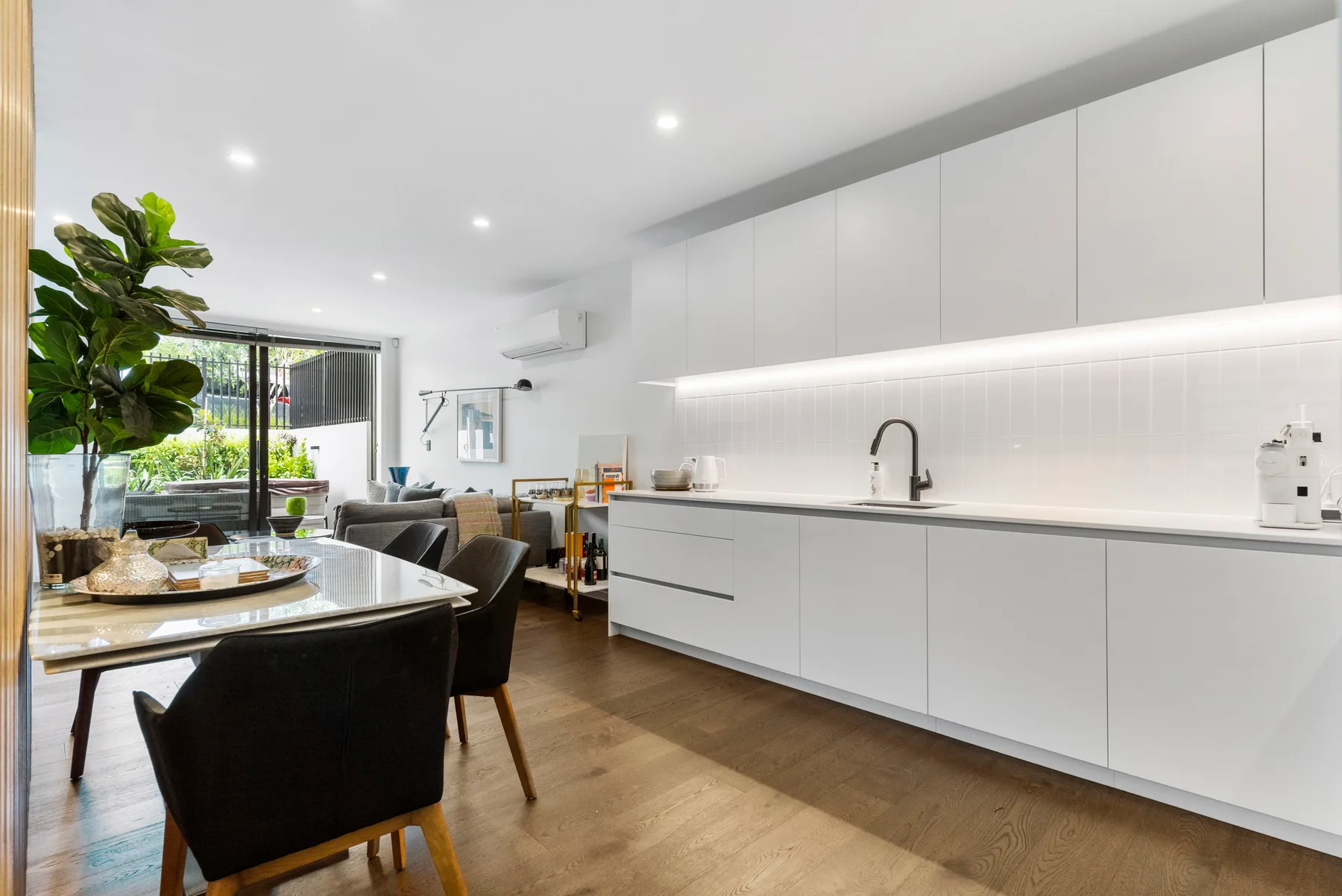 A bright open-plan kitchen and dining area with white cabinetry and a dining table.