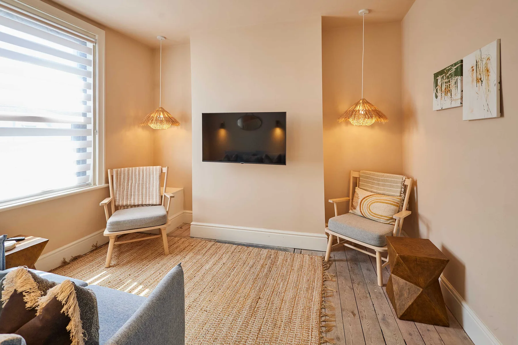 Una sala luminosa con un televisor en la pared y asientos junto a una ventana grande.