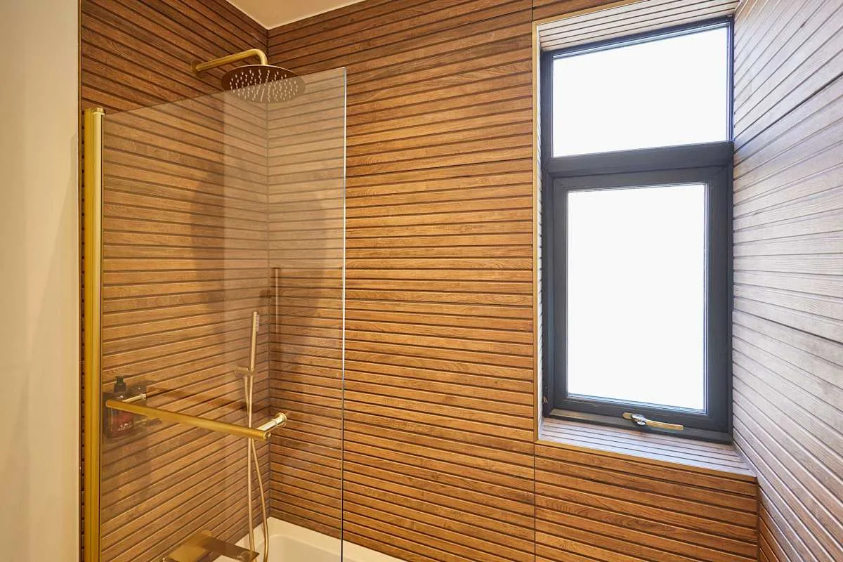 Una zona de ducha con paredes revestidas de madera y una ventana alta.