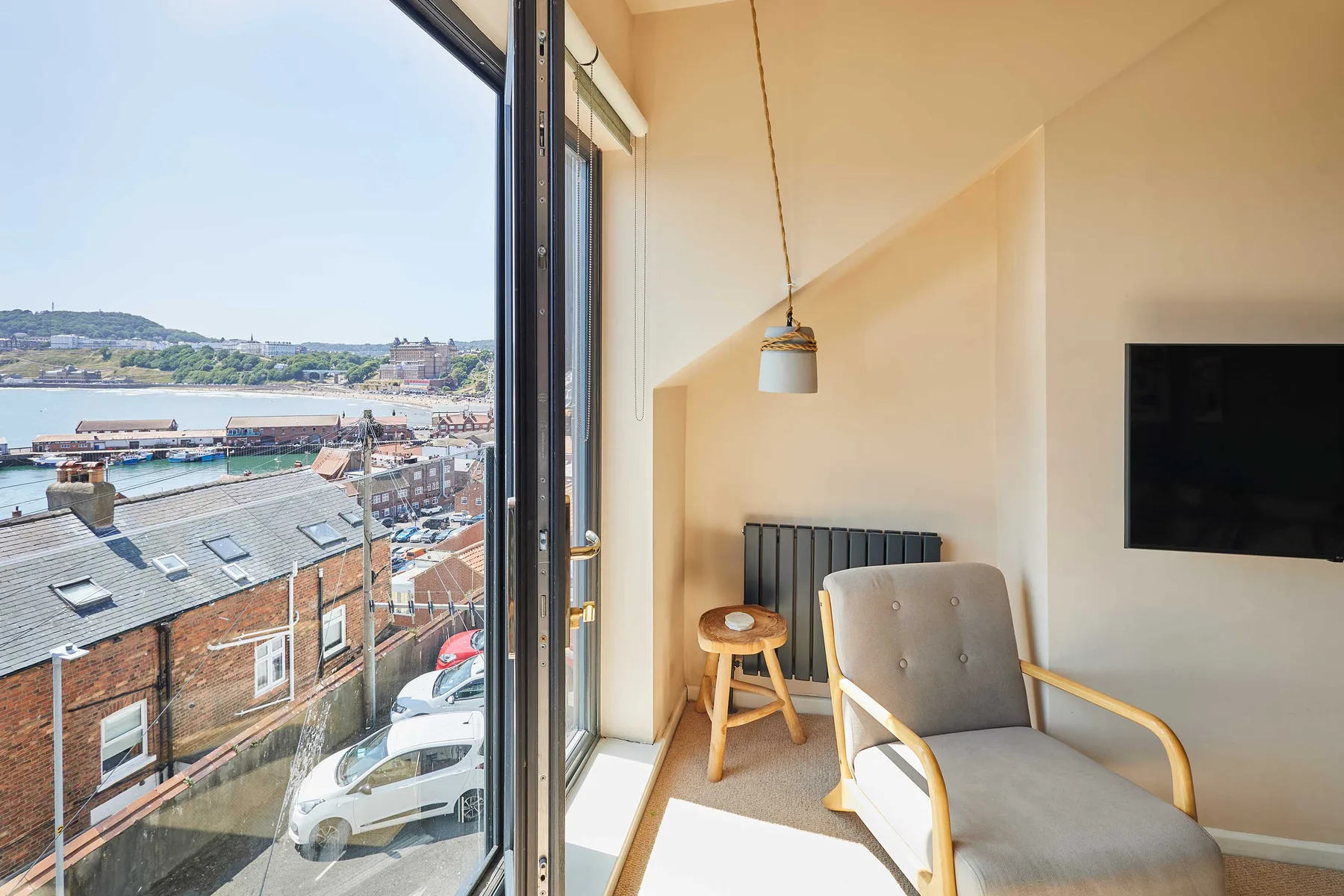 Una luminosa zona de estar con sillón, televisor y una gran ventana con vistas al puerto.