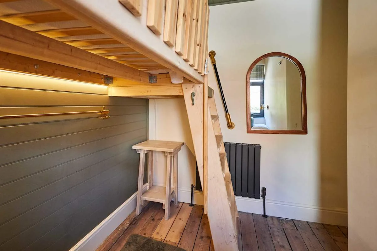 Una cama alta de madera con escalera y una mesa pequeña está en un dormitorio compacto.