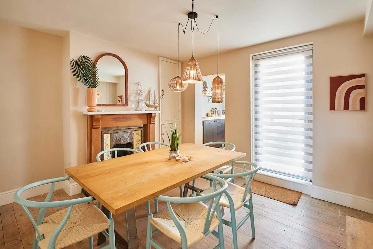 Comedor con mesa de madera, sillas claras y lámparas colgantes.