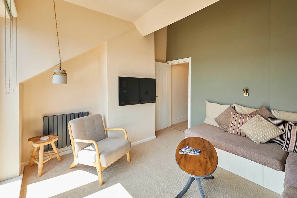 Un dormitorio con una cama, un sillón tapizado y un televisor montado en la pared.