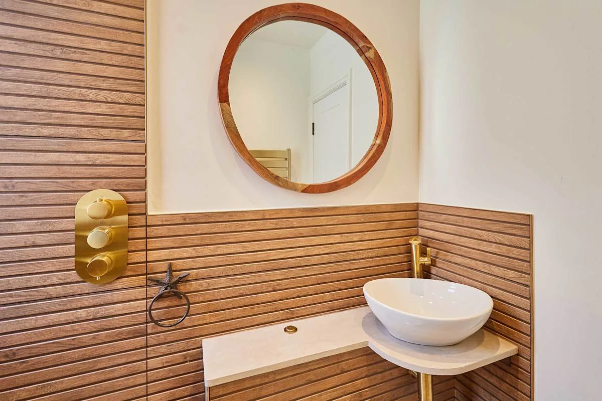 Un tocador de baño con un espejo redondo y un lavabo blanco sobrepuesto.