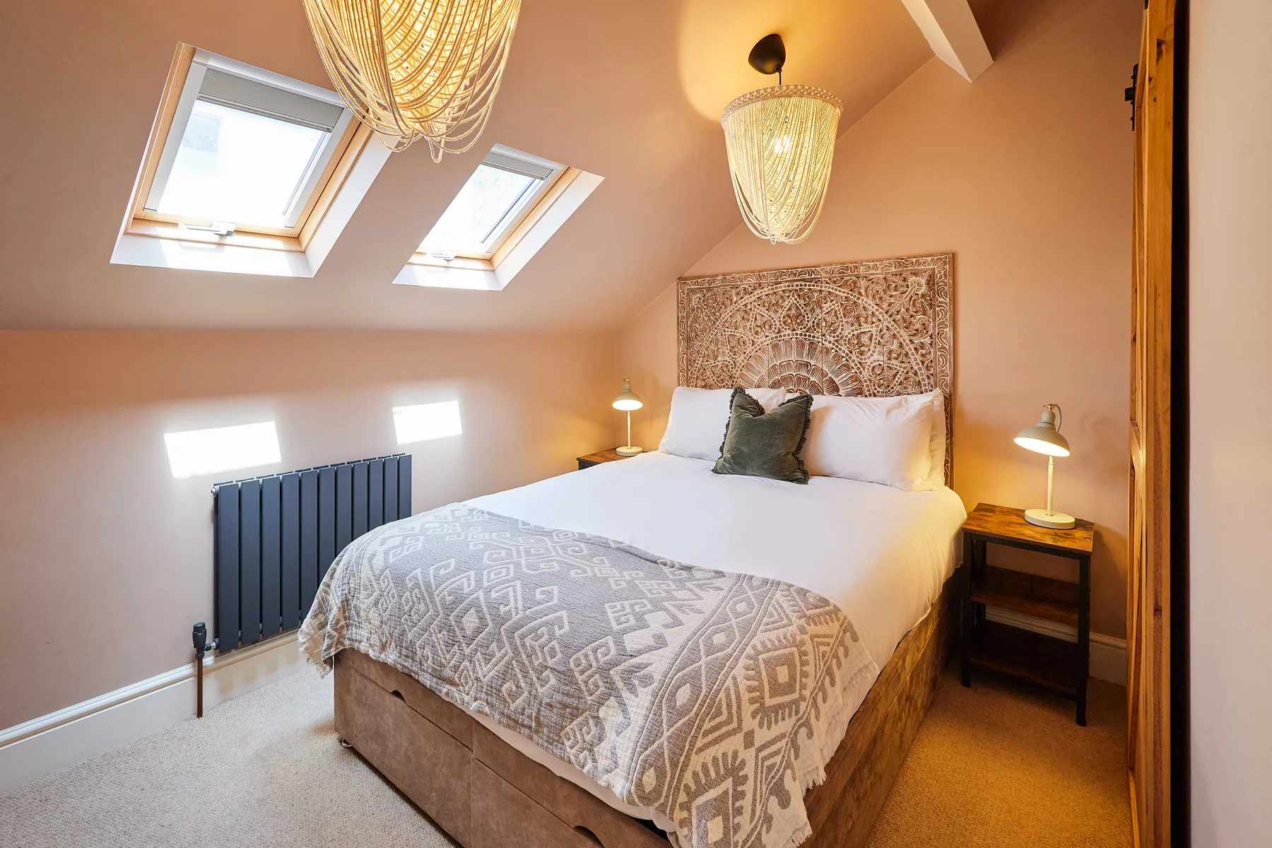 A bedroom with a double bed beneath two skylights and warm pendant lights.