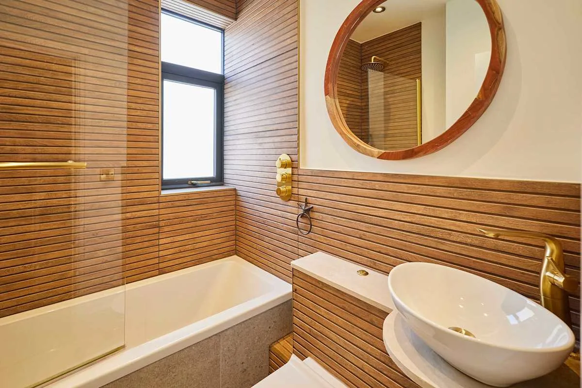 Un baño con bañera, lavabo de sobreponer y espejo redondo.