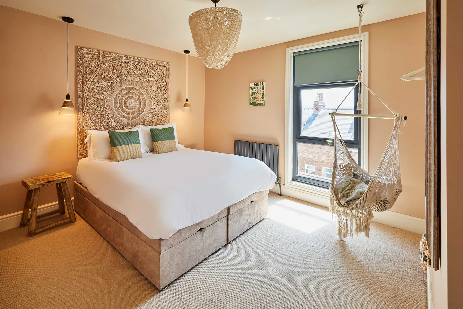 A bedroom with a bed, patterned wall hanging, and hanging chair by the window.