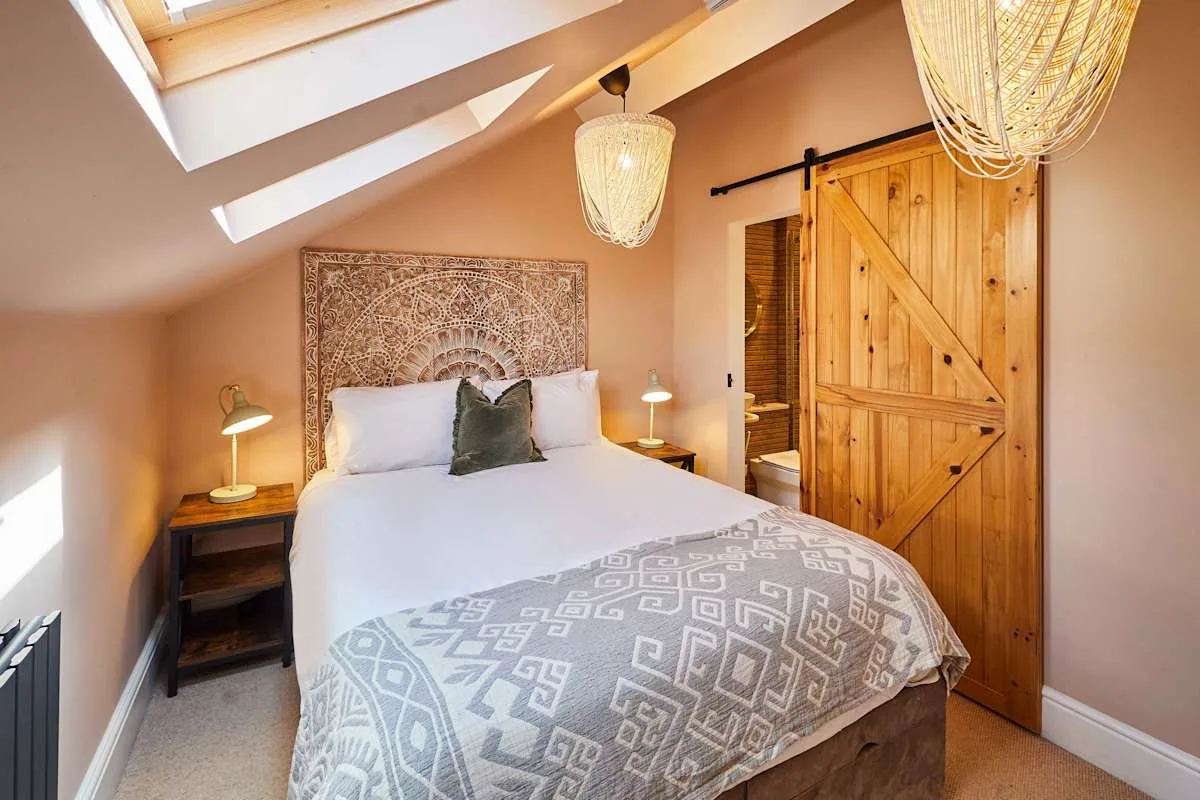 Un dormitorio con una cama bien arreglada, mesitas de noche y una puerta corrediza de madera.