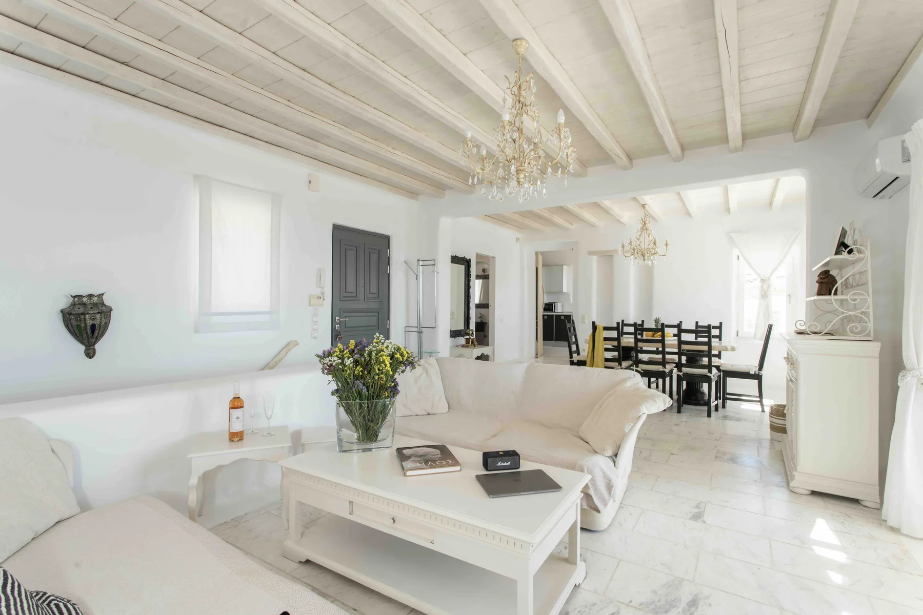 A bright living room opens onto a dining area, with white seating and a coffee table.