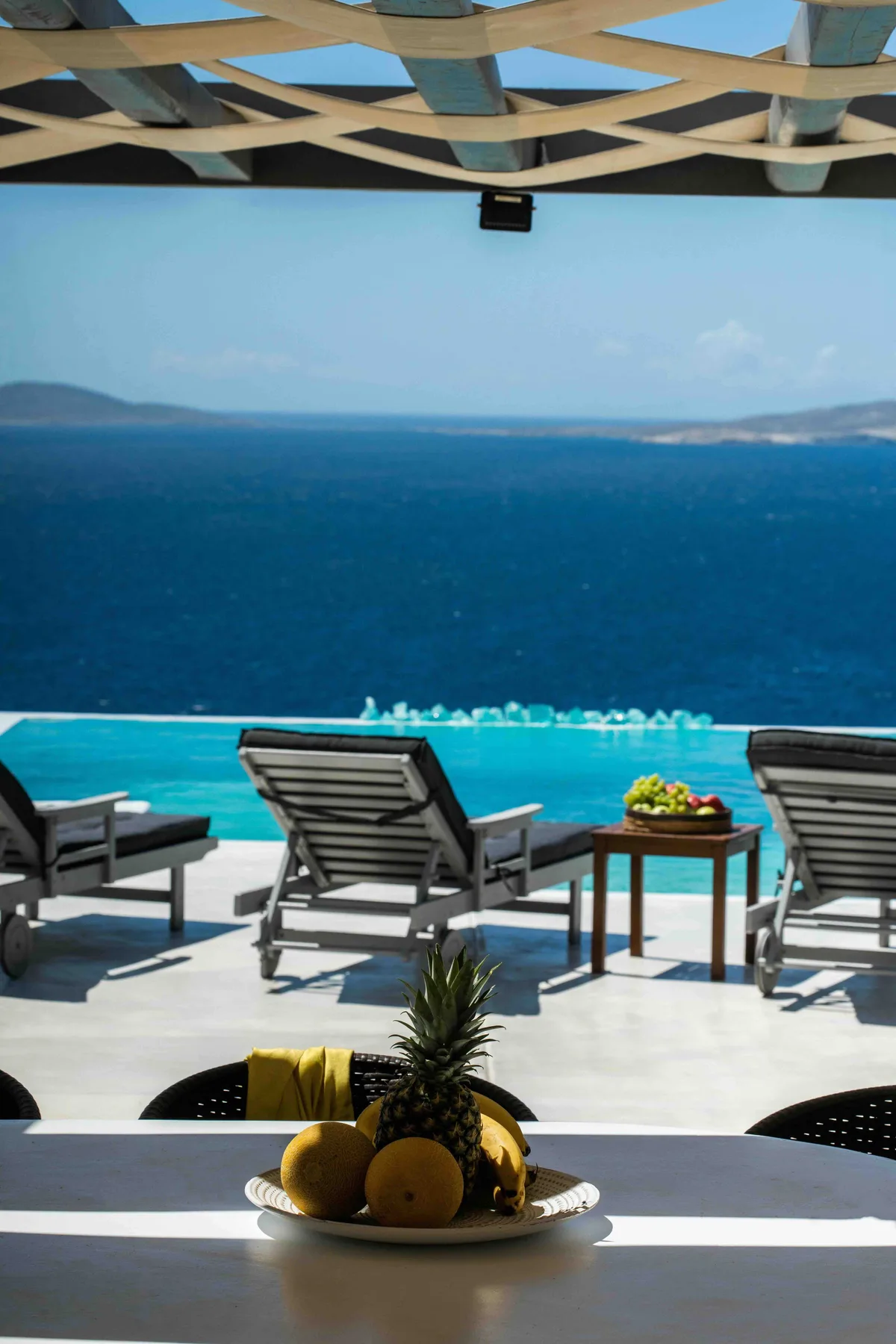 A seaside terrace with lounge seating overlooks a turquoise pool and the ocean.