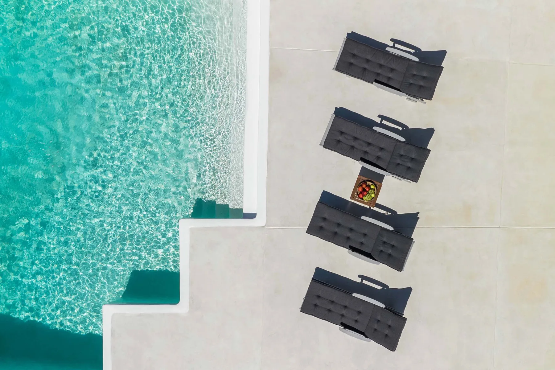 Poolside lounge chairs sit beside turquoise water.
