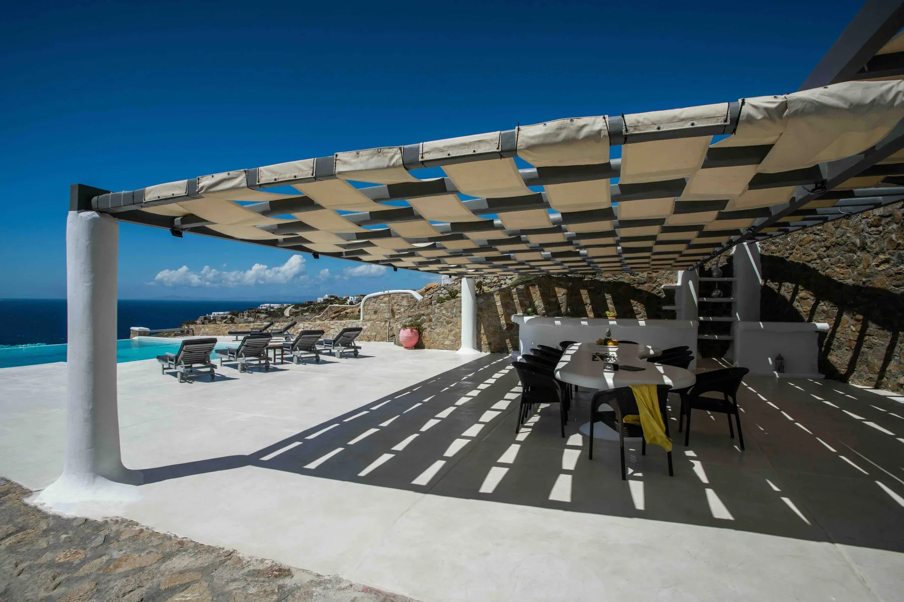 A seaside patio has outdoor seating beneath a striped shade canopy.