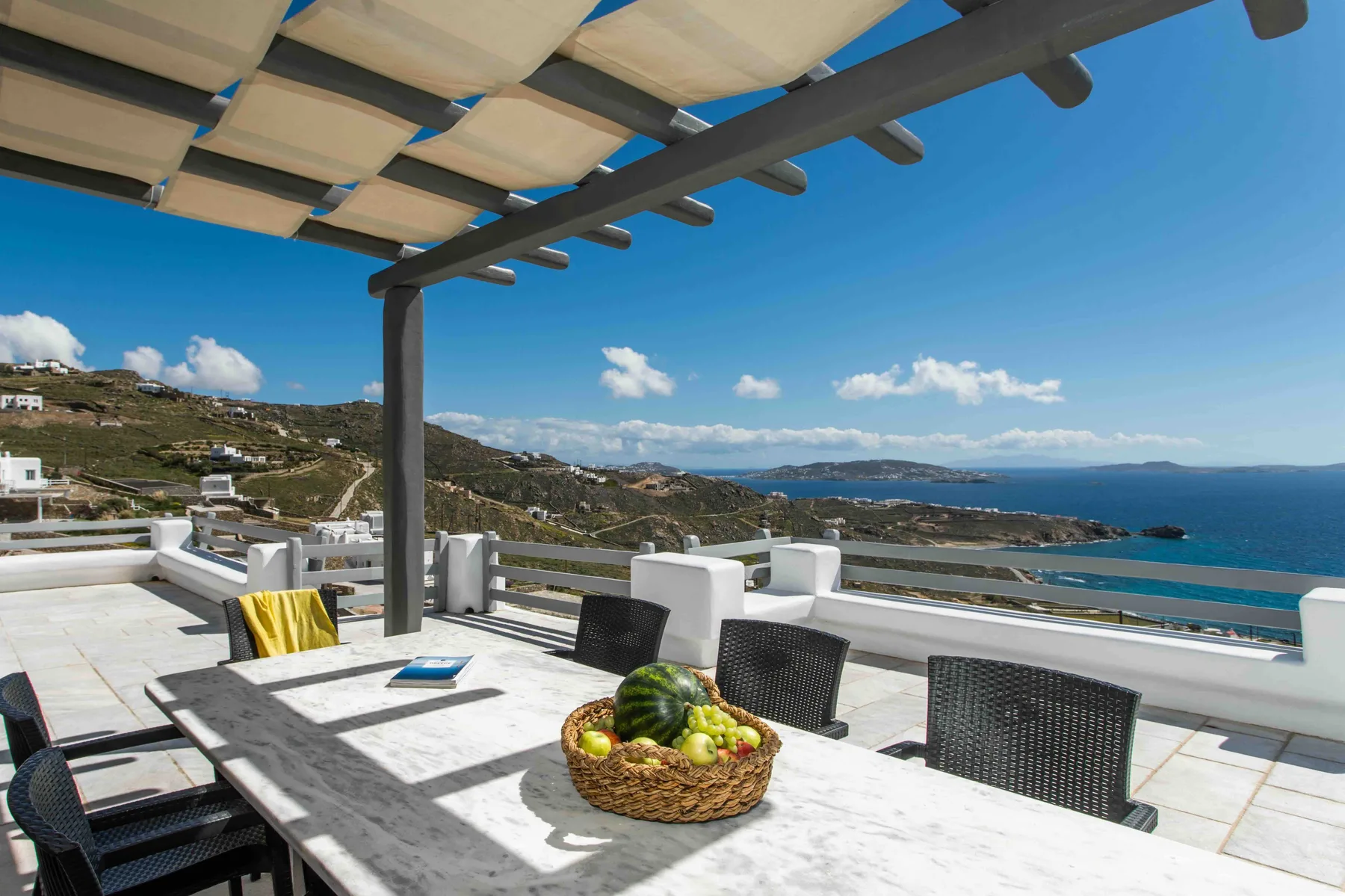 An outdoor dining terrace overlooks a coastal landscape and blue water.