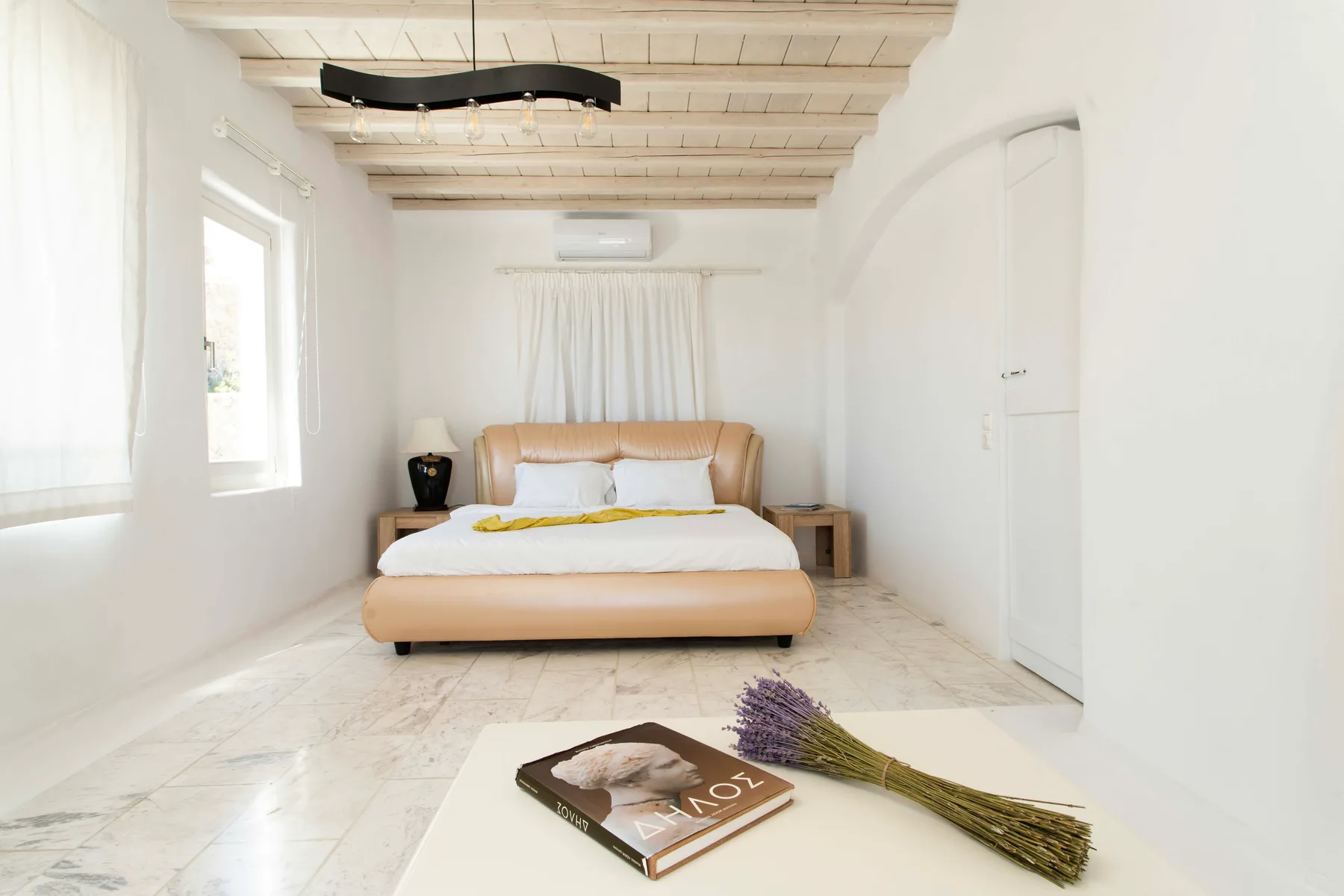 A bright bedroom with a bed beneath a pale exposed-beam ceiling.