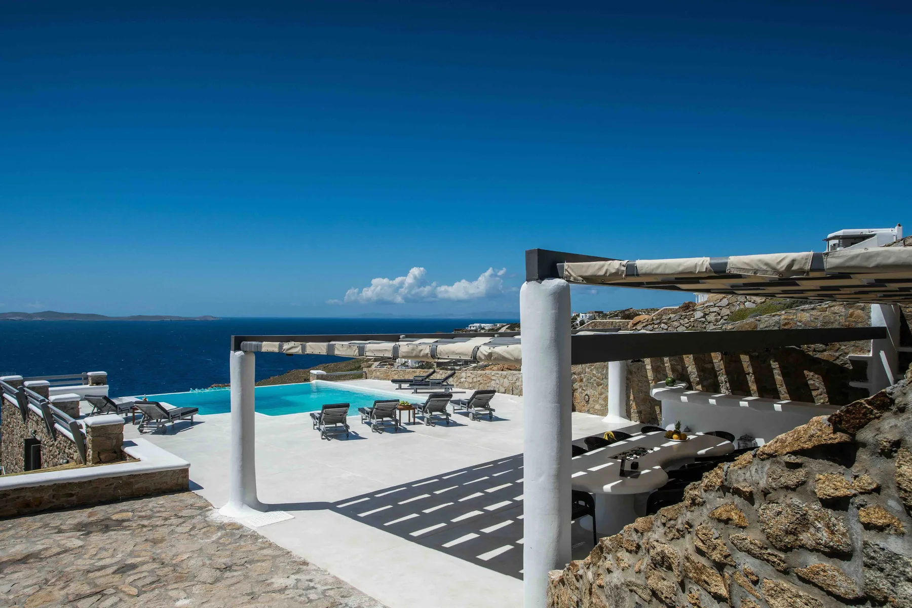 An outdoor pool terrace overlooks the sea, with lounge seating beside the water.
