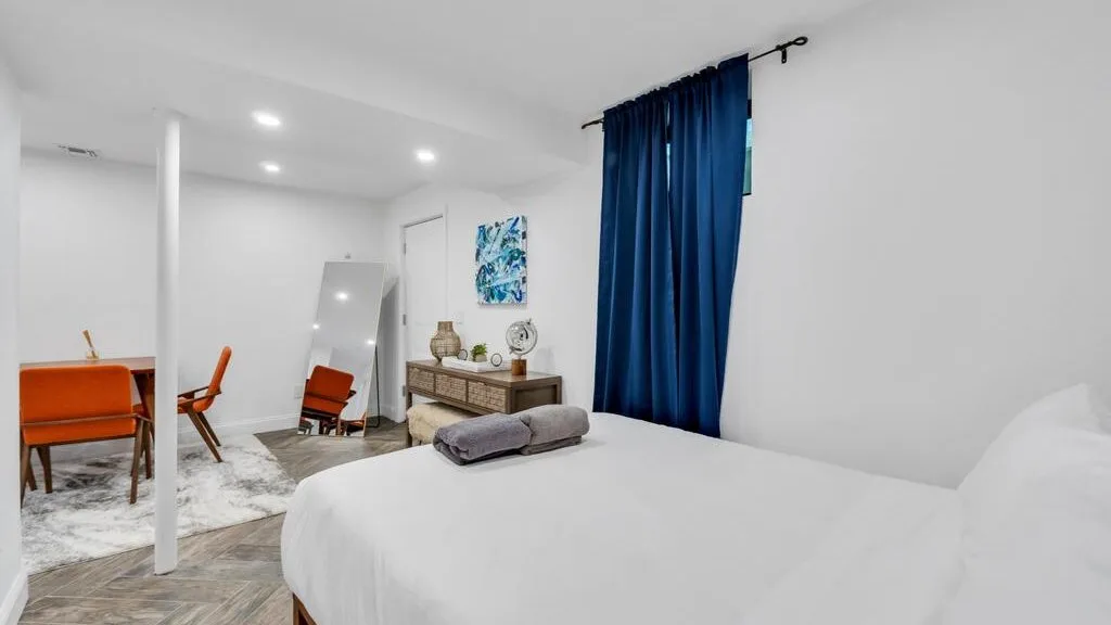 A bright bedroom with a large bed, blue curtains, and a small dining area.