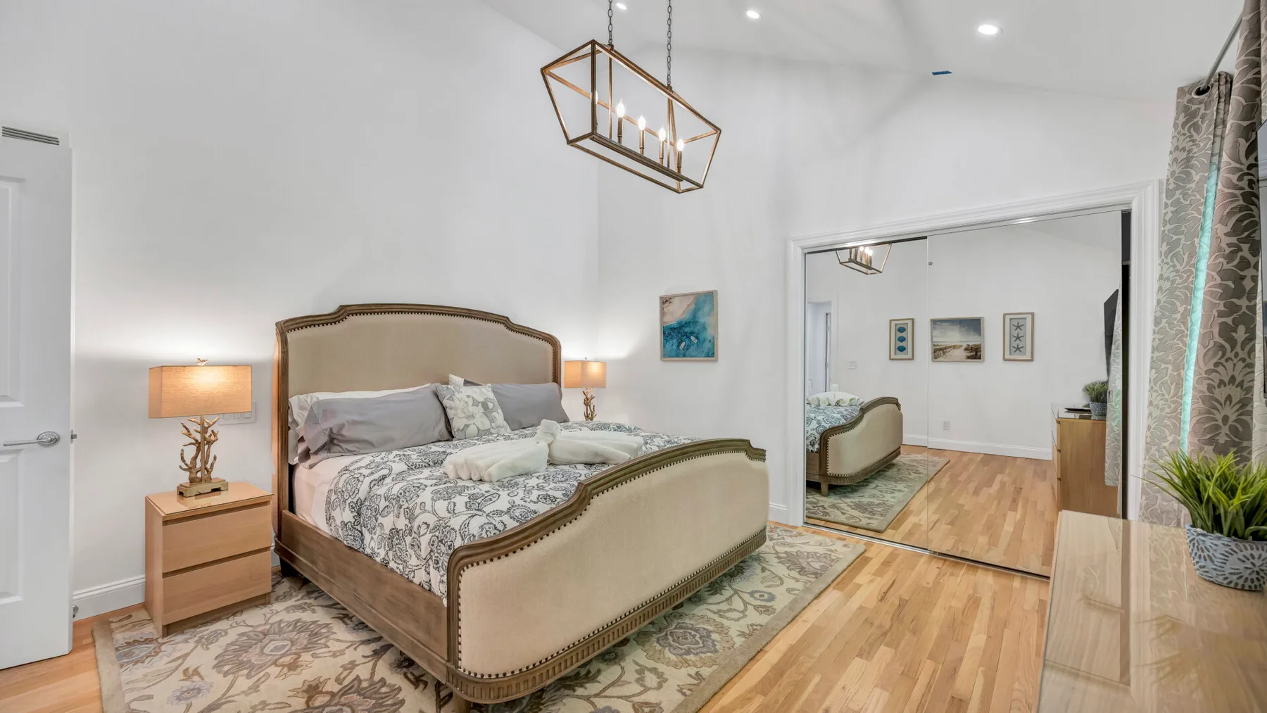 A bright bedroom with a large bed, bedside tables, and a patterned rug.