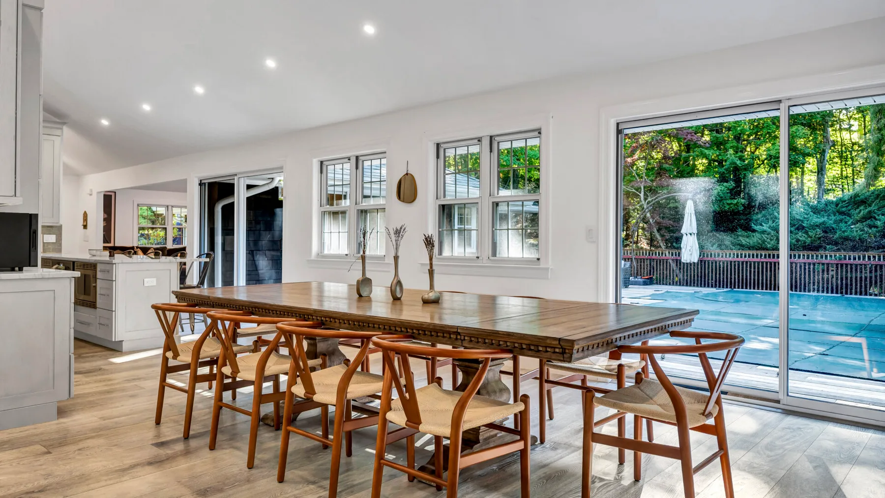 A bright dining area with a long wooden table and large windows overlooking a pool.