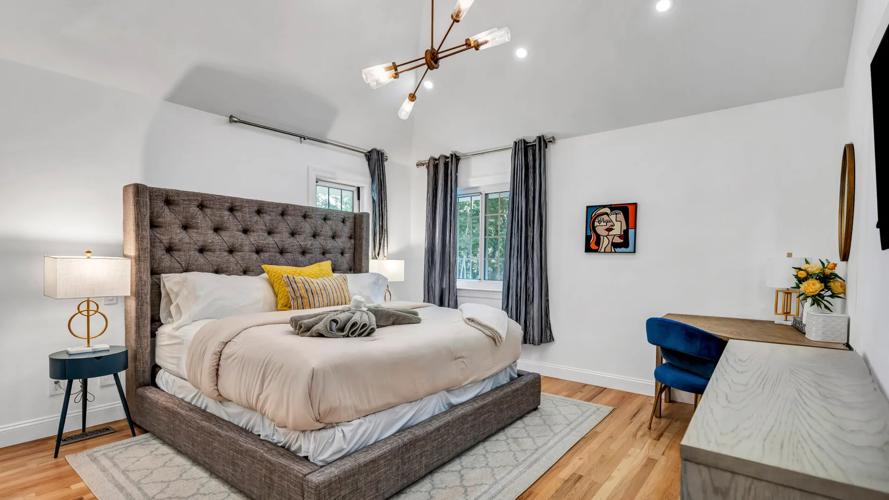 A bright bedroom with a large bed, bedside tables, and tall windows.