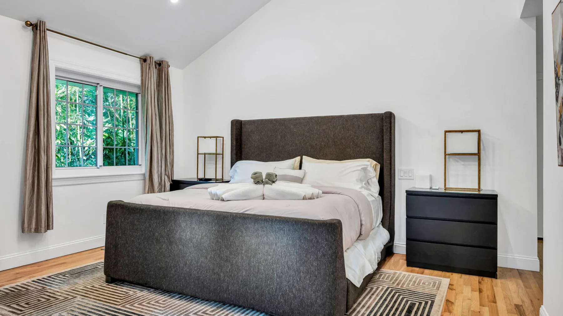 A bedroom with a large bed, a window, and wooden flooring.