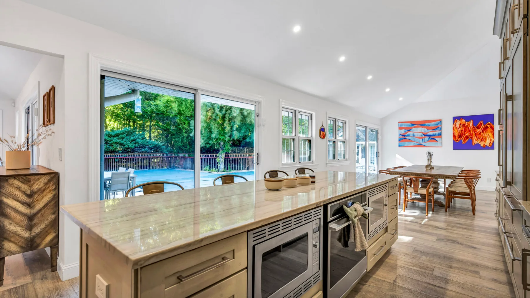 A bright kitchen and dining area with a long island and windows overlooking greenery.