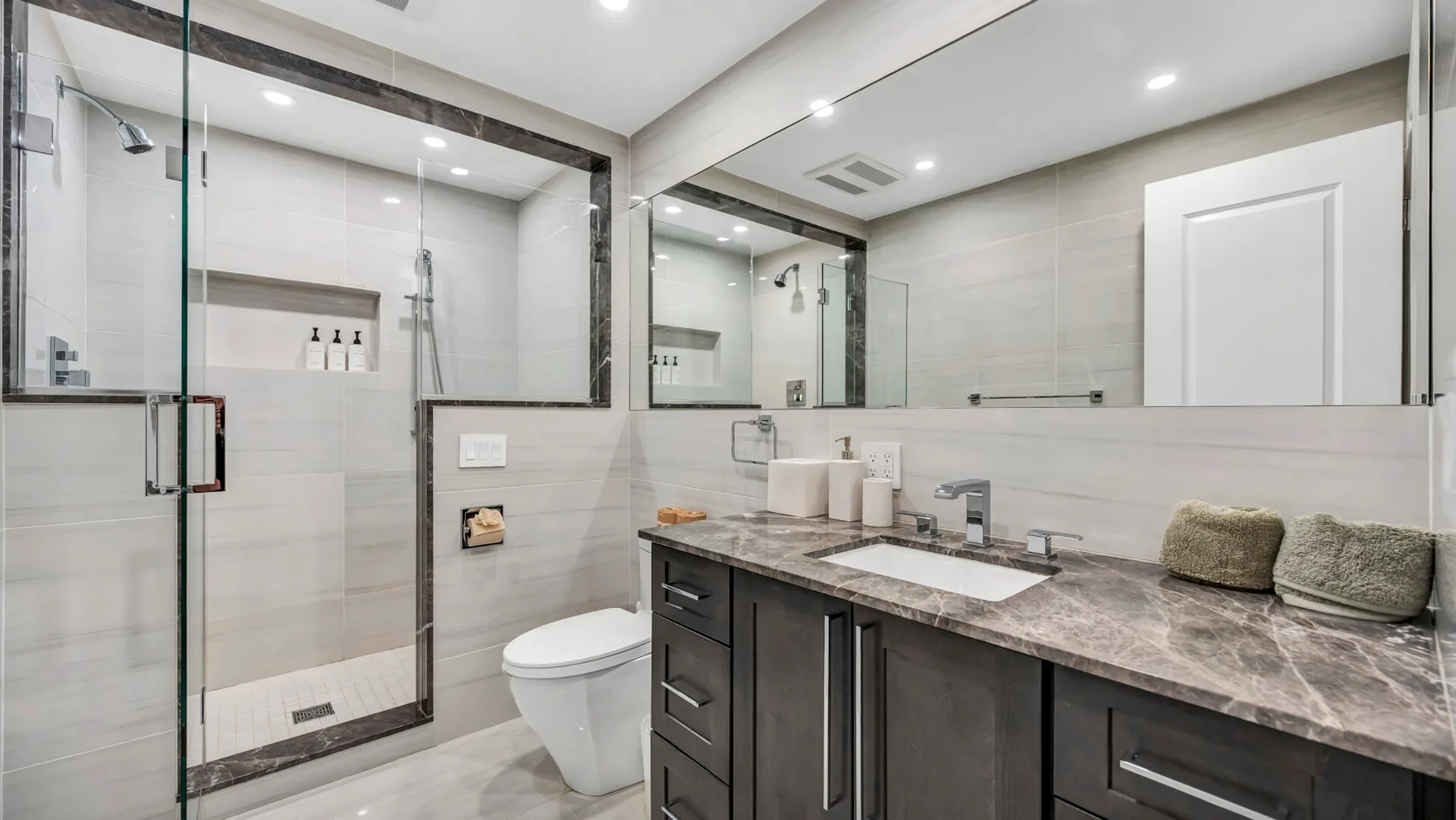 A bright bathroom with a glass shower, a sink, and a long vanity.