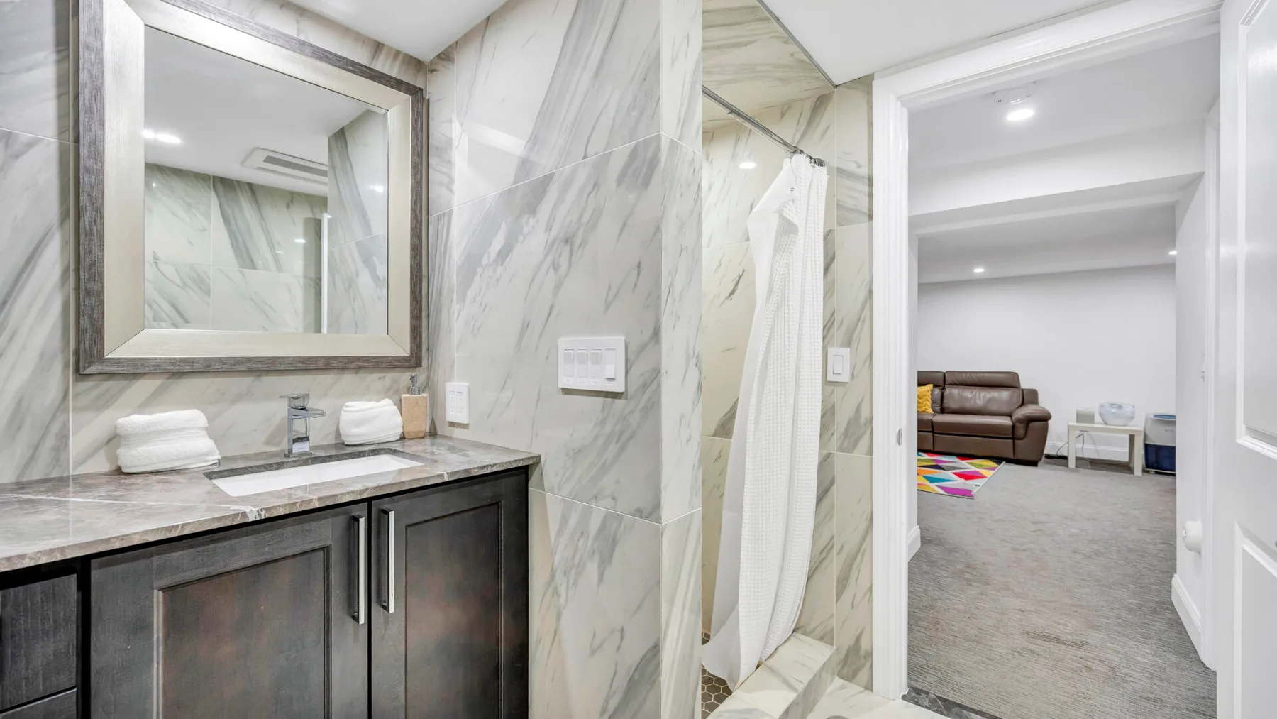 A marble bathroom vanity and shower open onto a carpeted room with seating.